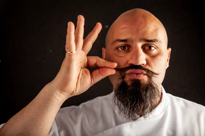 Carlo Guerriero in giacca da chef, sorride e si liscia i baffi